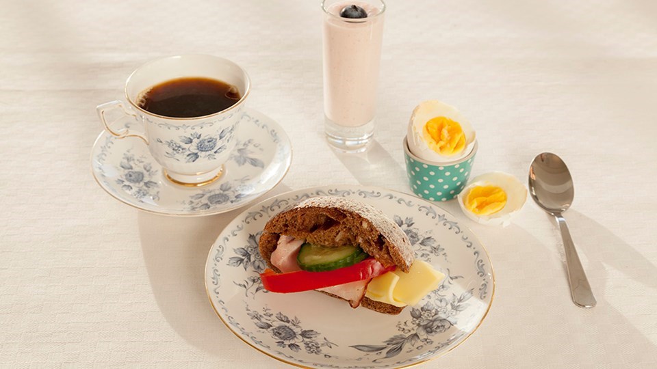Kaffe, grov smörgås med pålägg, ägg och smoothie upplagt på ett fint sätt.